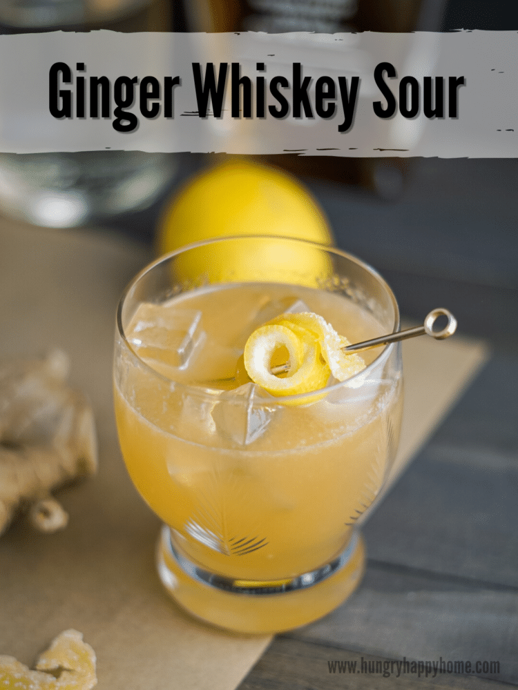 Ginger whiskey sour in a antique crystal glass garnished with lemon peel and candied ginger.