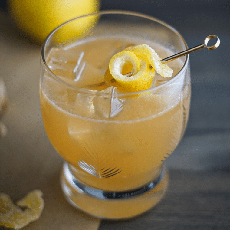 Ginger whiskey sour in a antique crystal glass garnished with lemon peel and candied ginger.