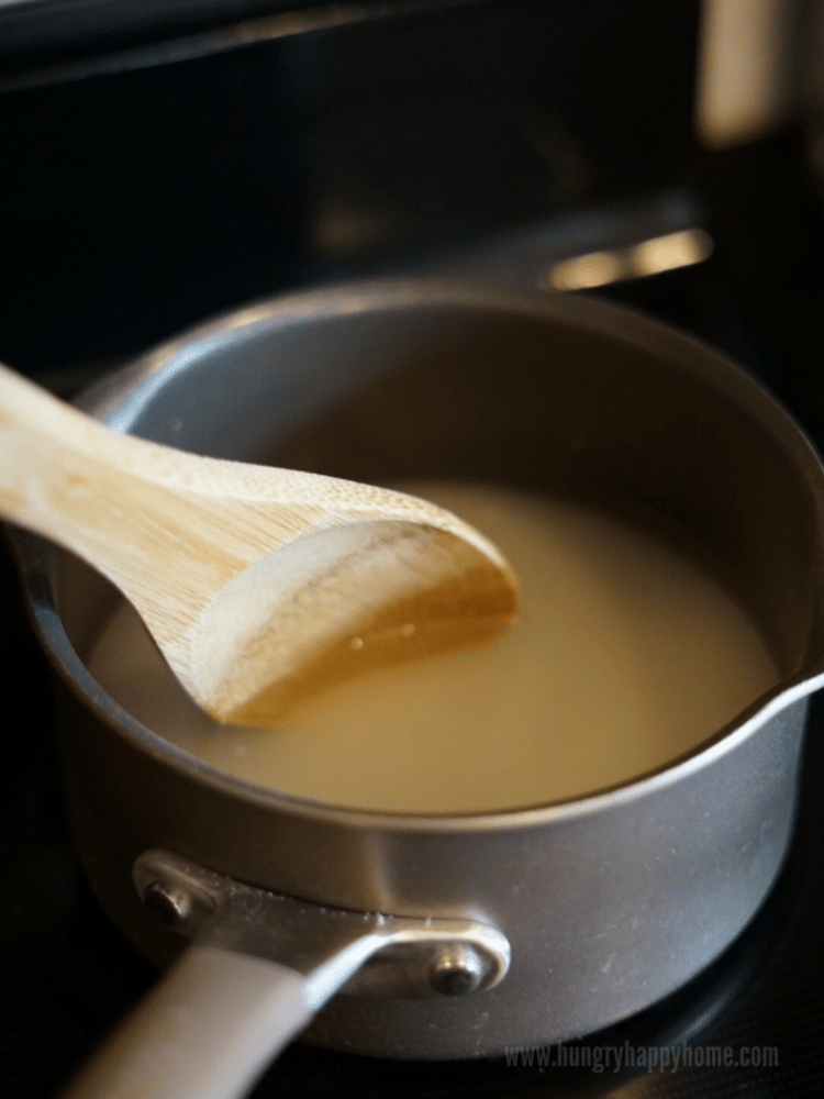 Sugar and water being stirred by a wooden spoon. It is in small sauce pan on the stove.