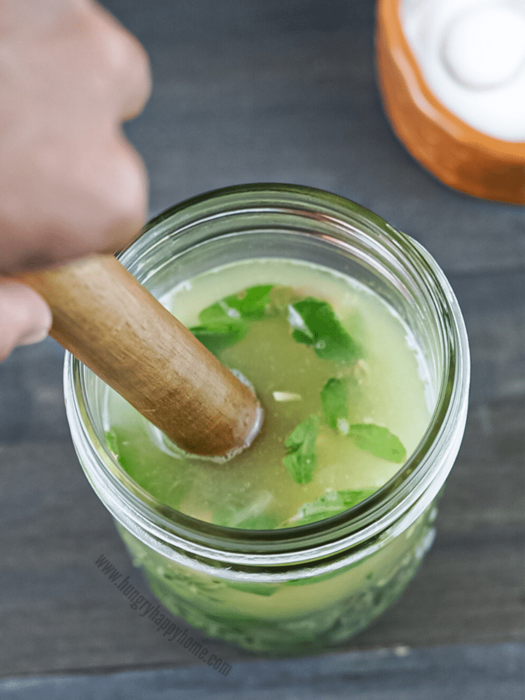 Fresh lemon juice and fresh sweet basil leaves being muddled in a glass mason jar.