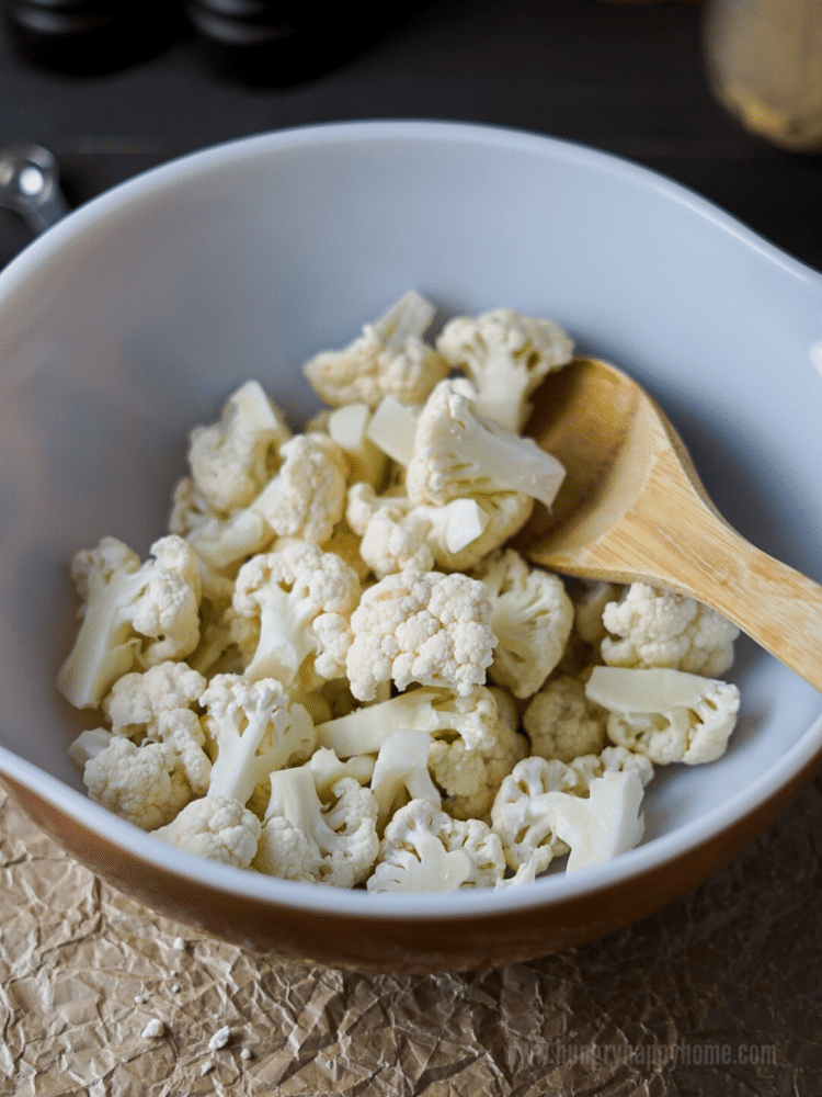 Pyrex bowl filled with raw cauliflower florets. A wooden spoon is resting in the bowl.