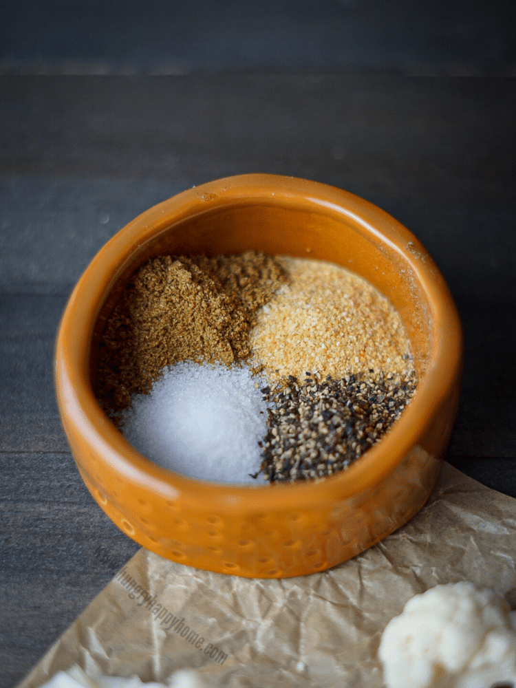 Small ceramic bowl with salt, pepper, cumin, and garlic powder spices in it.