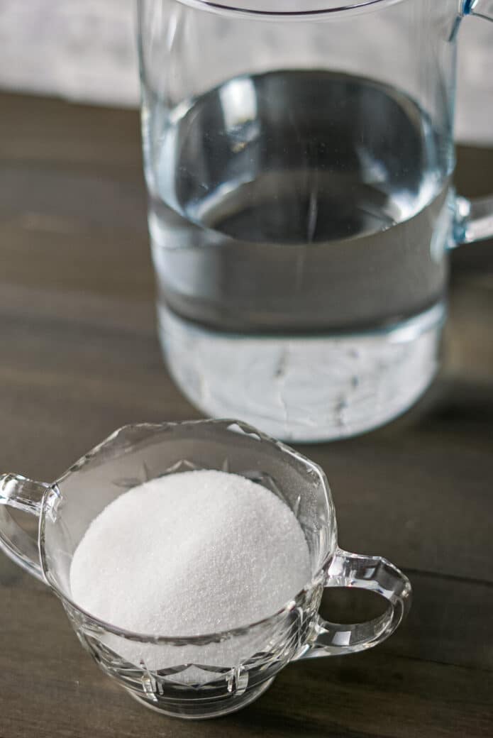 A bowl of sugar and a clear glass pitcher of water on a wooden table.