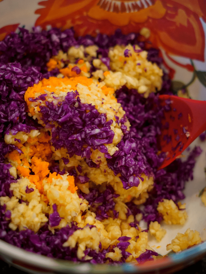 Ingredients for slaw being stirred in a floral bowl.