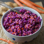Brightly colored Ginger Apple Slaw made with red cabbage in a ceramic bowl.