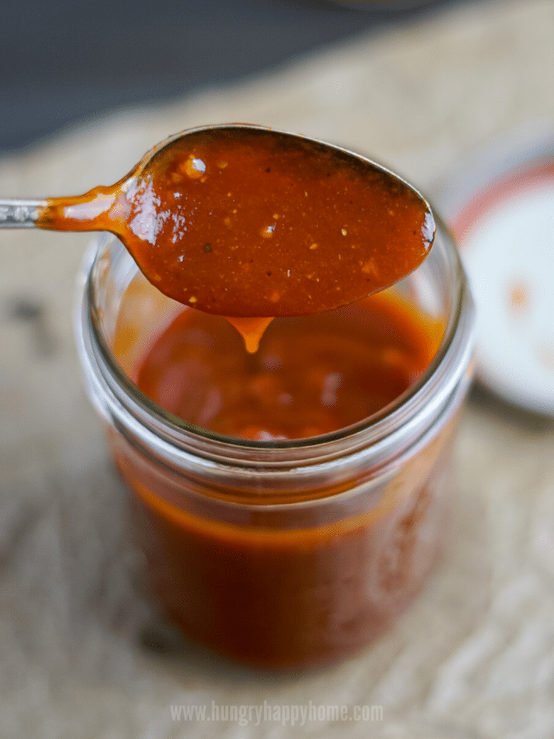 Bourbon Maple BBQ Sauce being poured from a spoon into a glass mason jar.