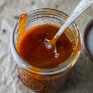 Maple Bourbon BBQ Sauce in a glass mason jar with a spoon.