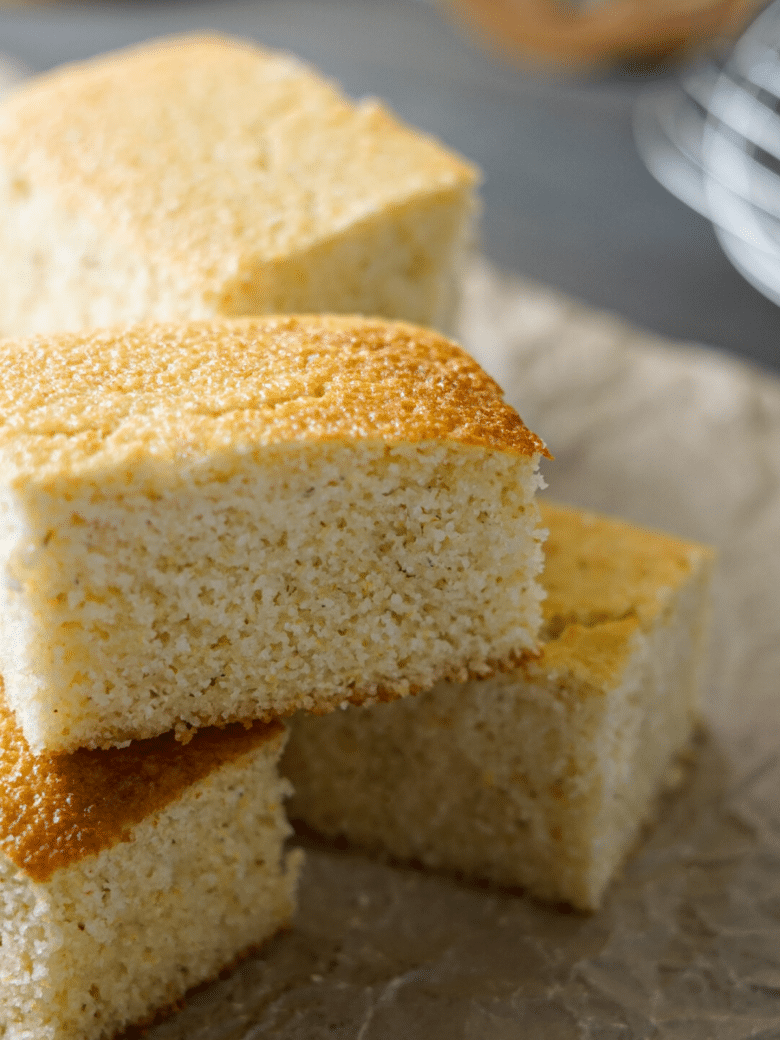 Squares of cornbread stacked on brown parchment paper.