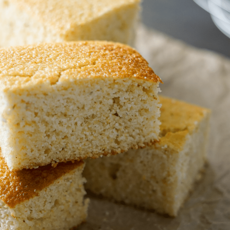 Squares of cornbread stacked on brown parchment paper.