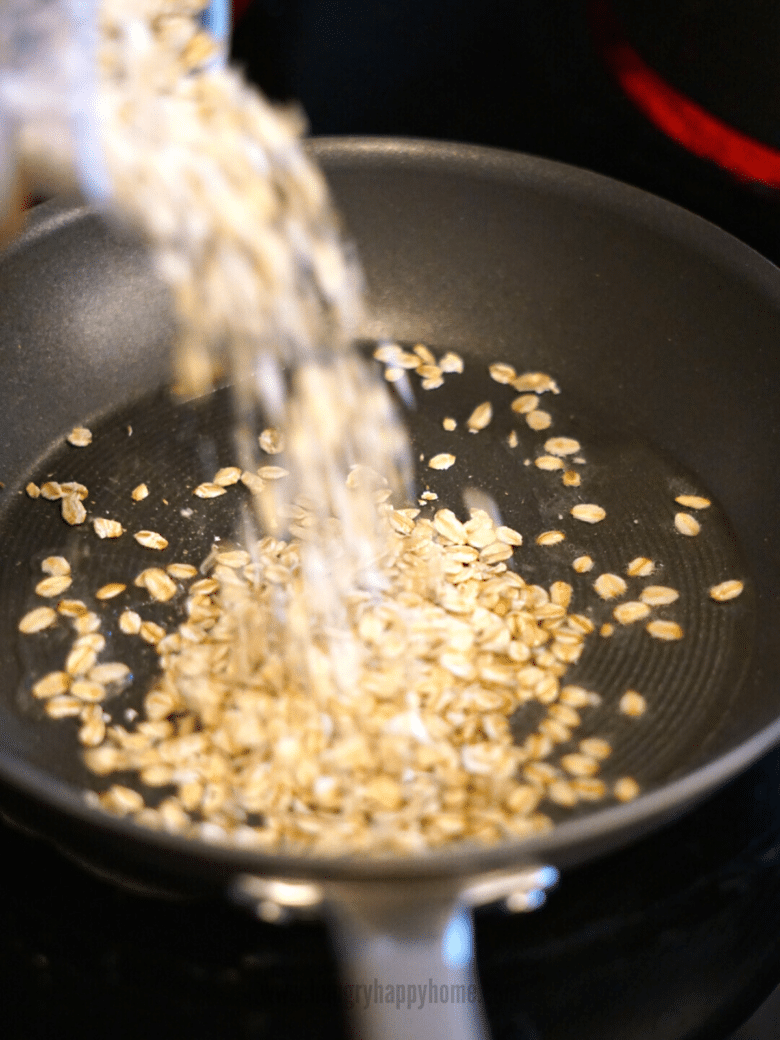 Raw rolled oats being poured into the pan with melted coconut oil.