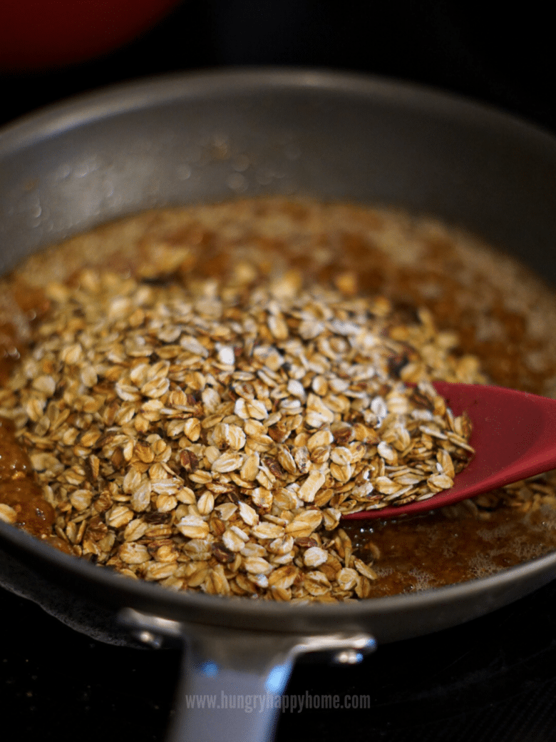 Oats and melted sugar mixture being combined in a pan on the stove.