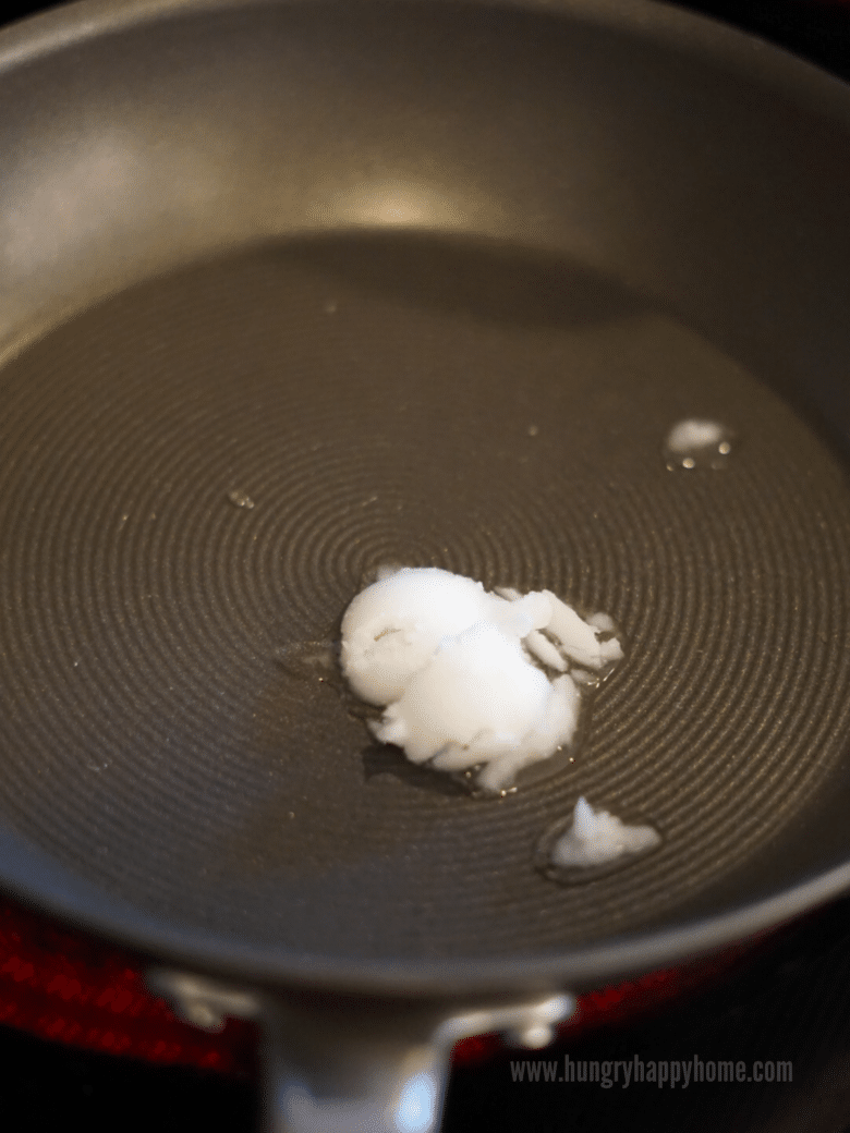 Coconut oil melting in a pan on the stove.