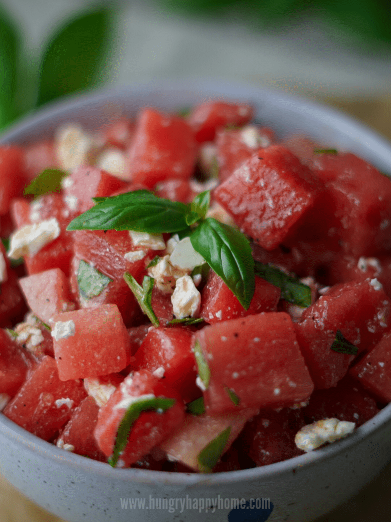 Watermelon Basil Salad with Feta in a blue ceramic bowl topped with a fresh sprig of sweet basil.