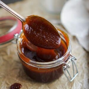 A small jar with BBQ sauce inside and a spoon scooping out BBQ Sauce.